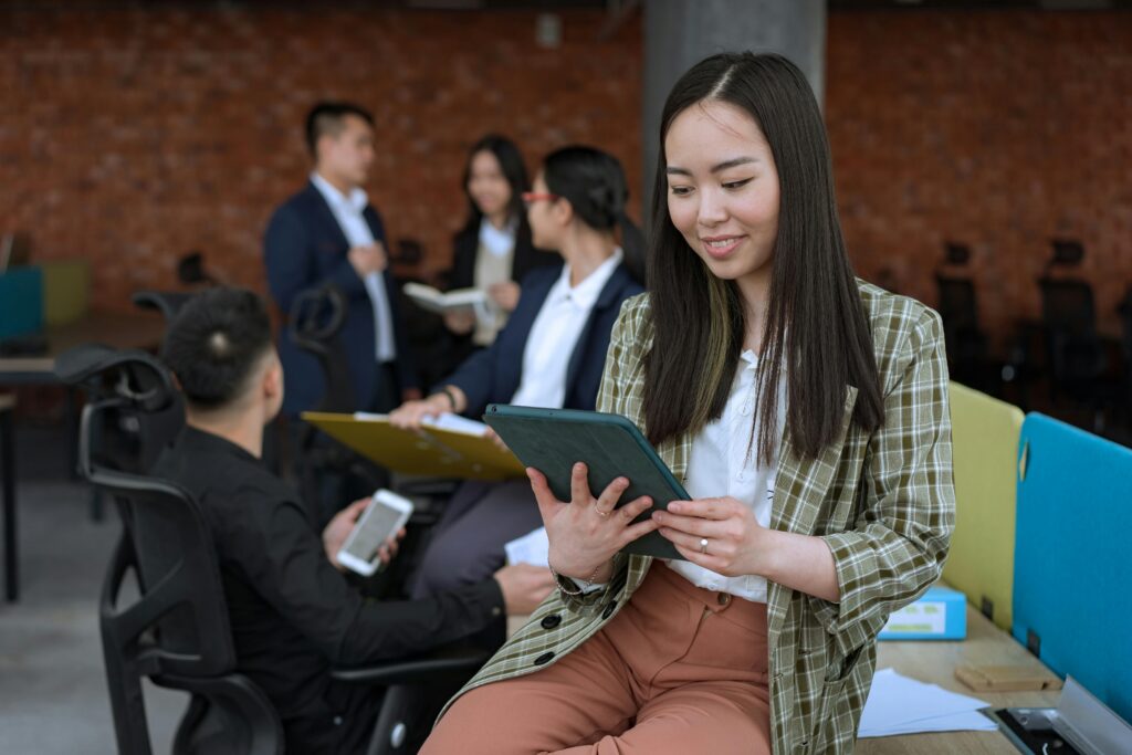 Young, Asian woman reading on her iPad, in a group setting of young professionals.