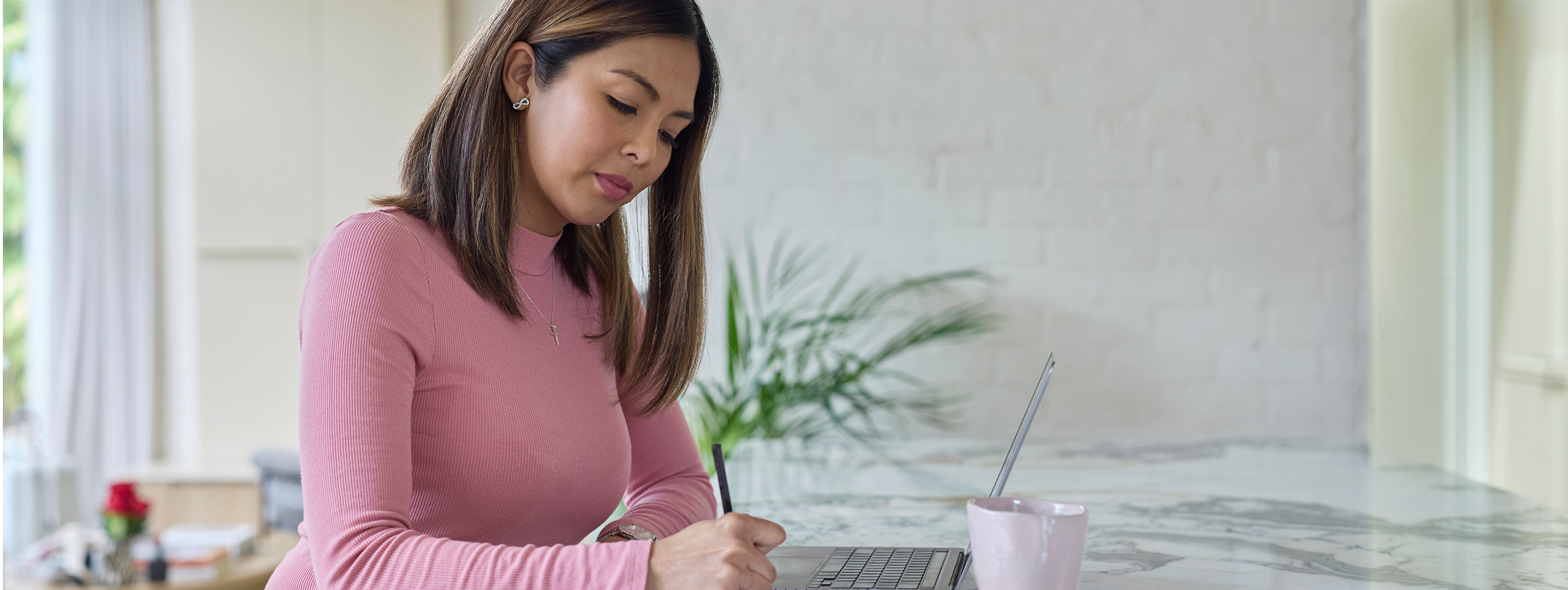 Young woman studying on her laptop in her kitchen with coffee.